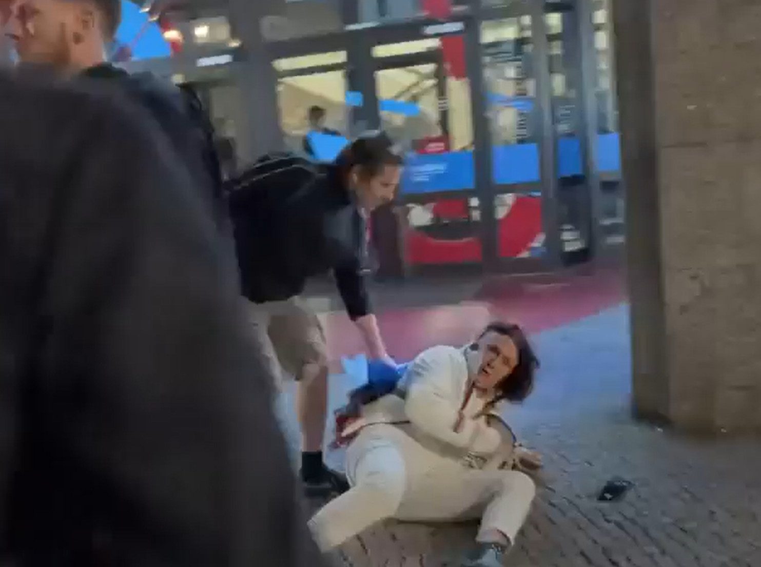 Anette am Boden, ein Helfer beugt sich zu ihr. Links: der beteiligte Polizeibeamte.